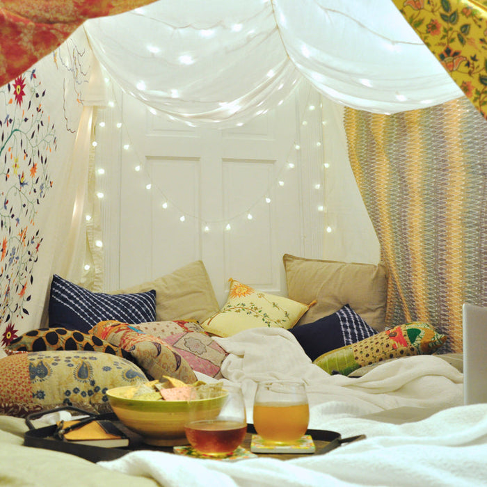 Blankets form a soft tent, with string lights draped in the background and pillows scattered around the floor.